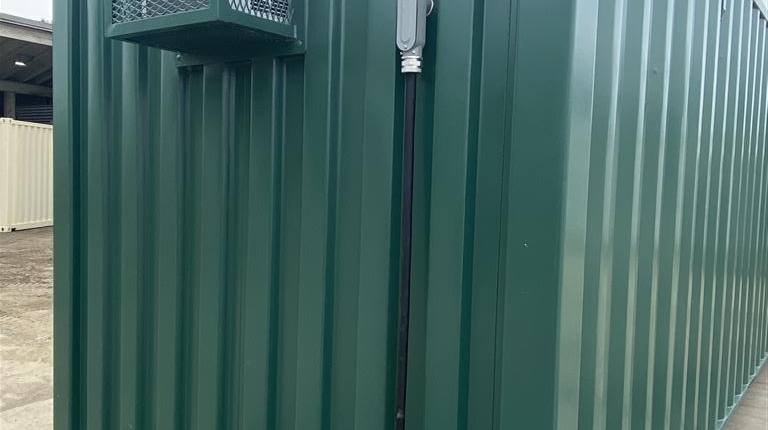 Photo shows the rear of a 20' shipping container, freshly painted in forest green according to the customer's request. Also shown is the custom built exterior cage holding the AC unit, as well as the electrical connection.