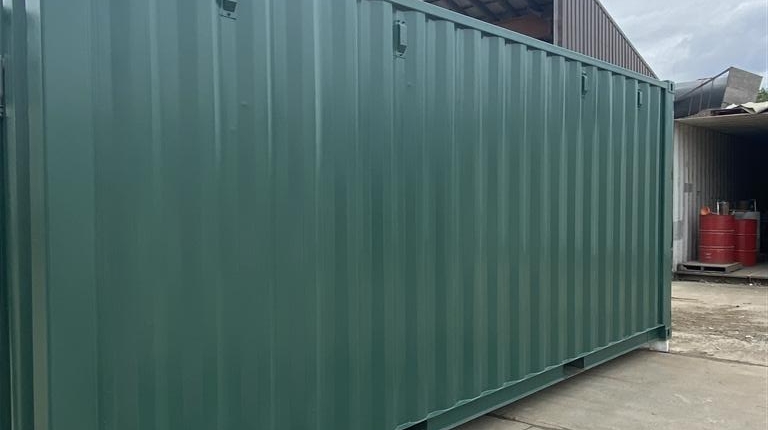 Photo shows a 20' steel shipping container from the front right corner, looking lengthway to rear of the container. The container has been freshly painted forest green according to the customer's specifications.