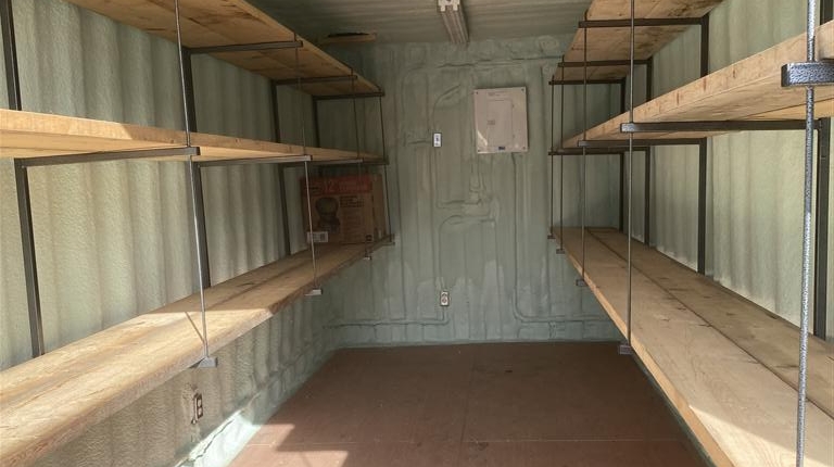 Photo shows interior of a shipping container with custom modifications including wood floor, 10 boards of 2" x 10" X 20' wood held on metal fabricated shelf brackets, per customer specifications. The container is insulated with spray foam, painted, and also includes 3 LED light fixtures with safety cages custom built.
